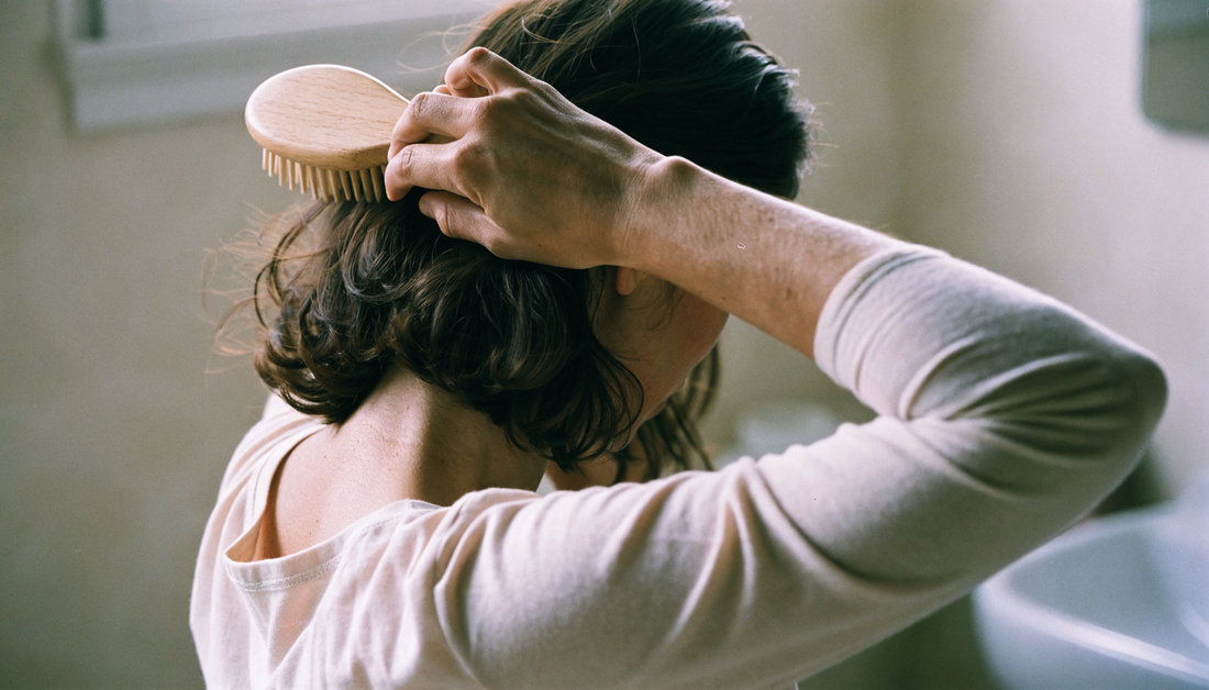 Femme brossant ses cheveux dans une salle de bain — chute de cheveux chez la femme